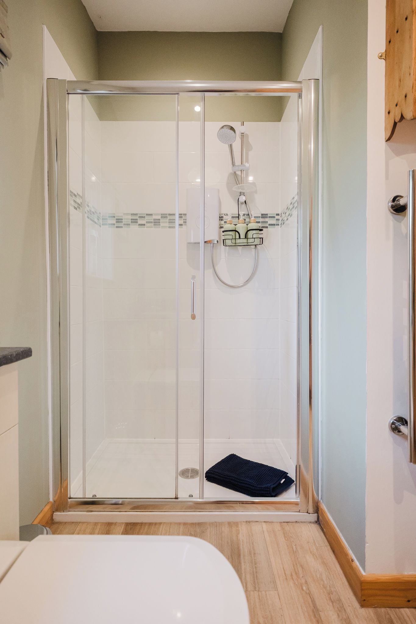 A glass-enclosed shower with a handheld showerhead and a towel rack.