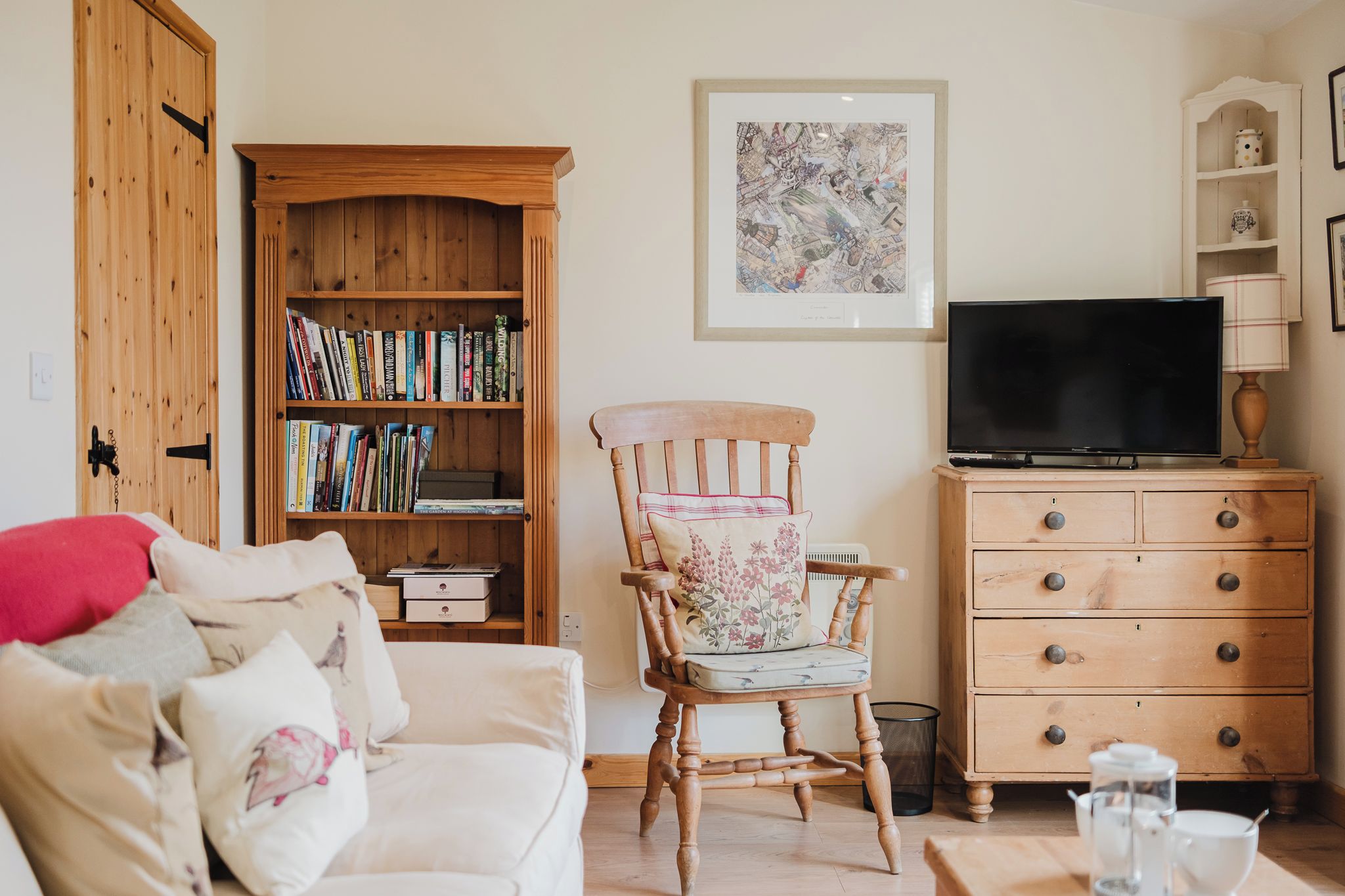 Un salon chaleureux avec une bibliothèque en bois, un téléviseur, un fauteuil à motifs floraux et un canapé blanc.
