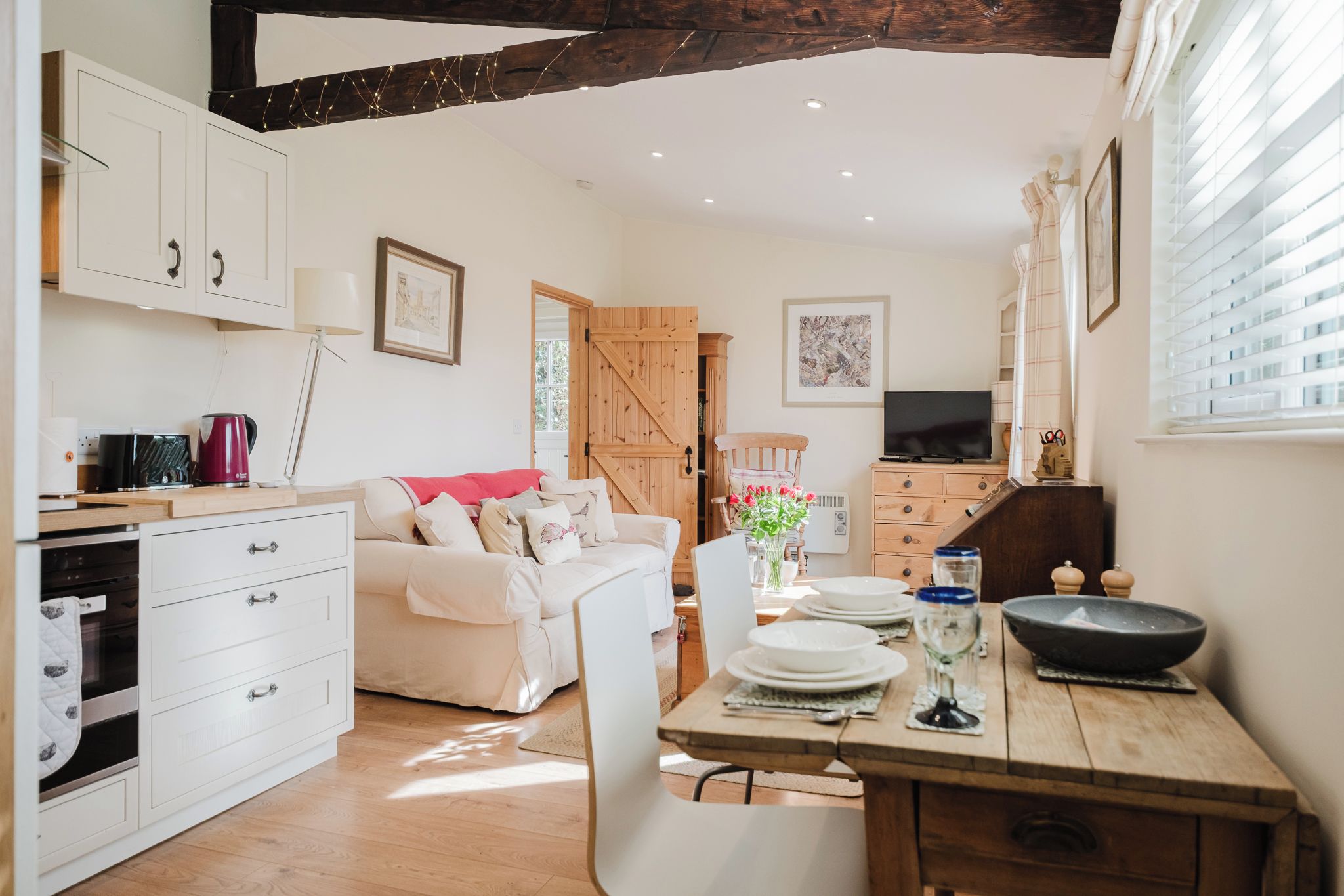 A cozy kitchen with a dining table set for two, a sofa, and a TV.