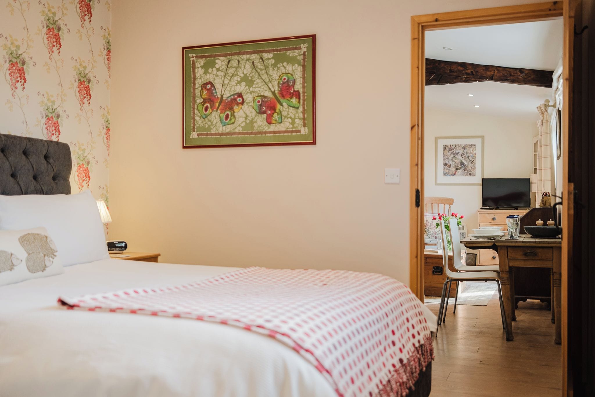 A bedroom with a bed, a desk, and a chair. There is a painting on the wall and a window.
