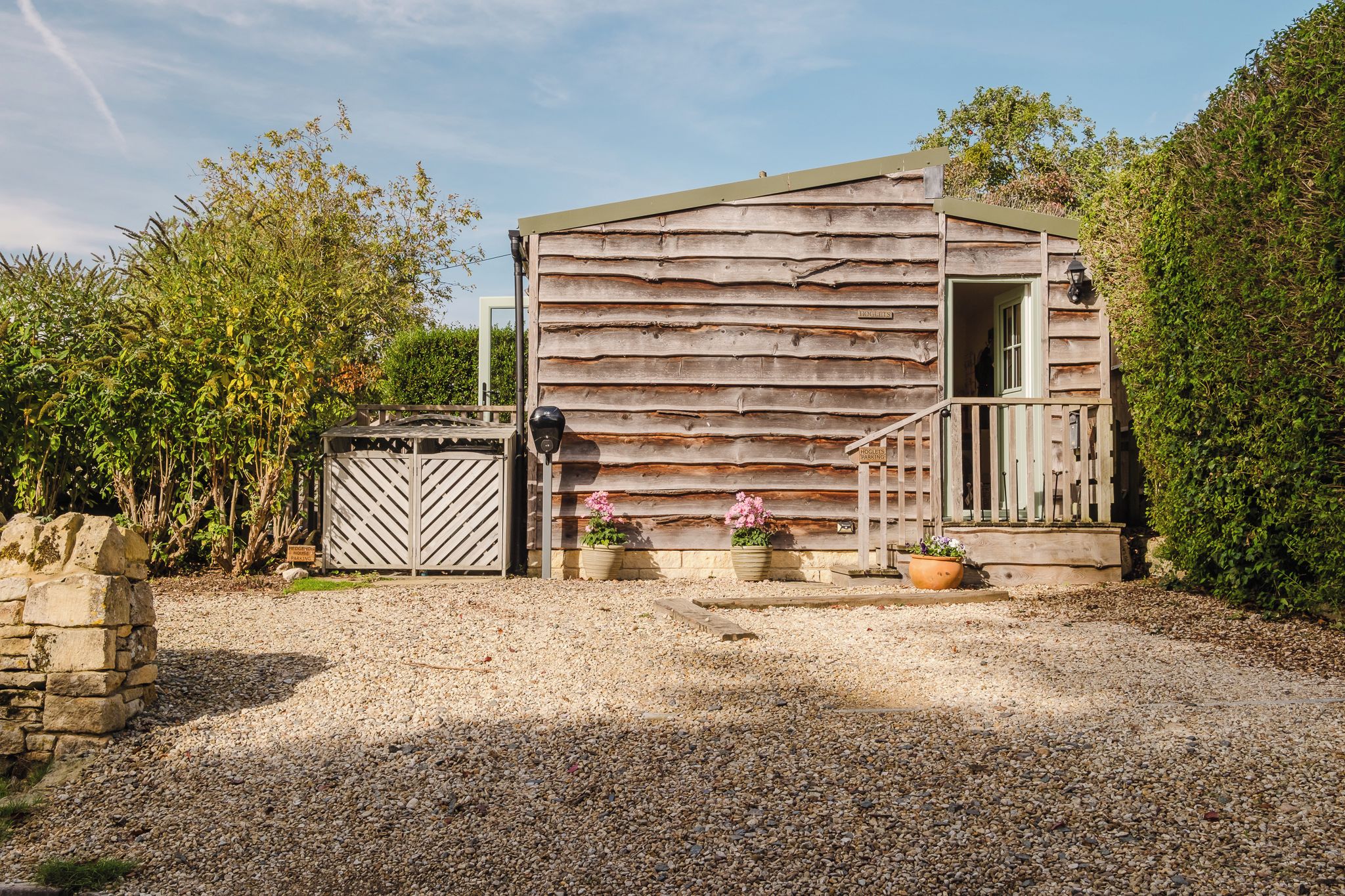 A rustic wooden building with a gravel driveway, a gated entrance, and potted plants.
