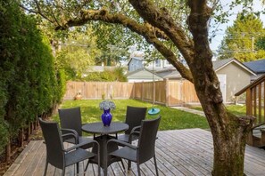 A patio with a round table and chairs, surrounded by a wooden deck and a tree. - Dunbar 2BR Homestay near UBC (Vancouver)
