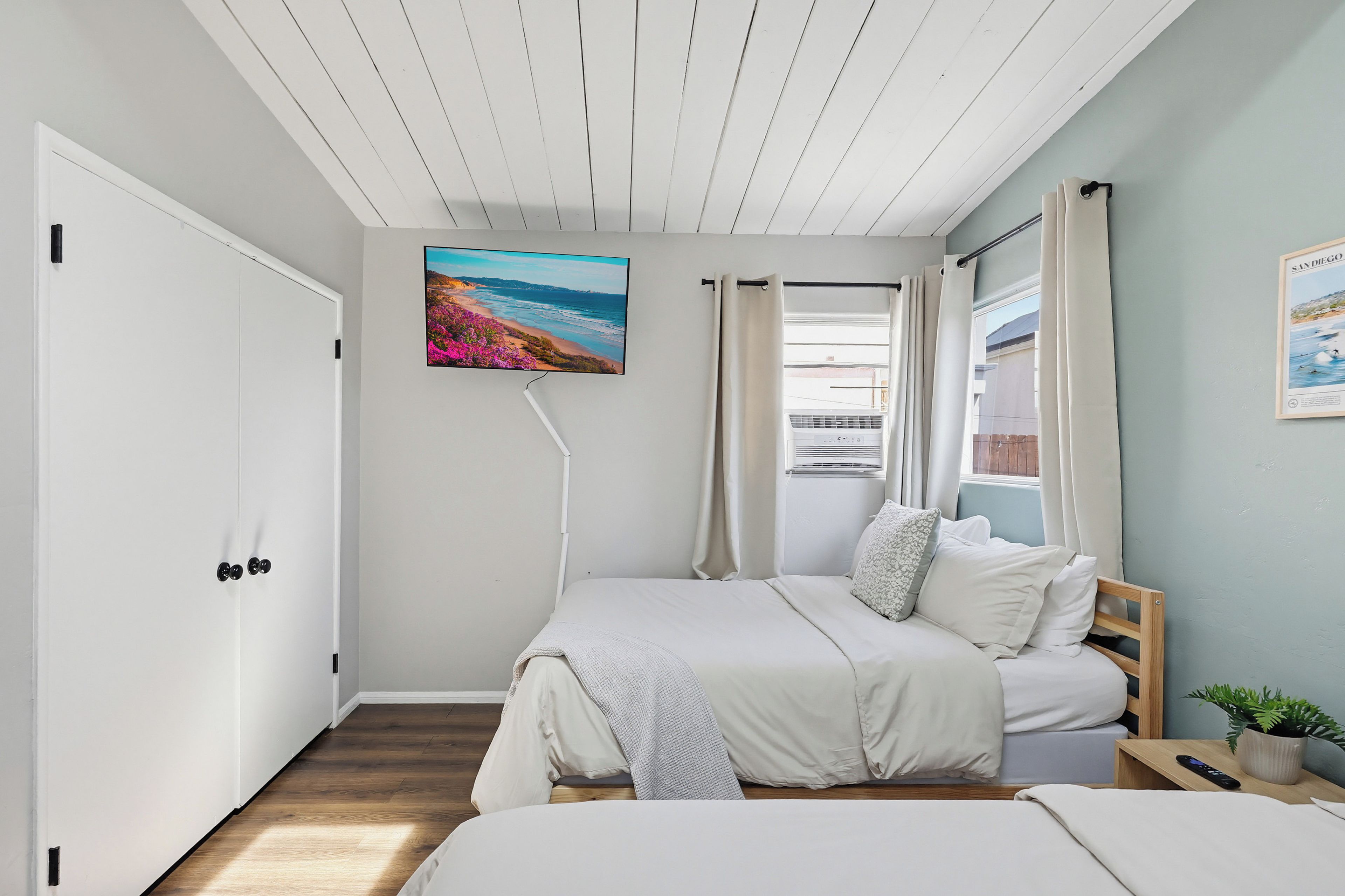A bedroom with a bed, a TV mounted on the wall, a window with curtains, and a door.