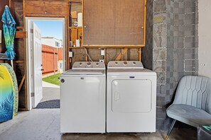 Une buanderie avec deux machines à laver blanches, un panneau perforé en bois et une chaise grise.