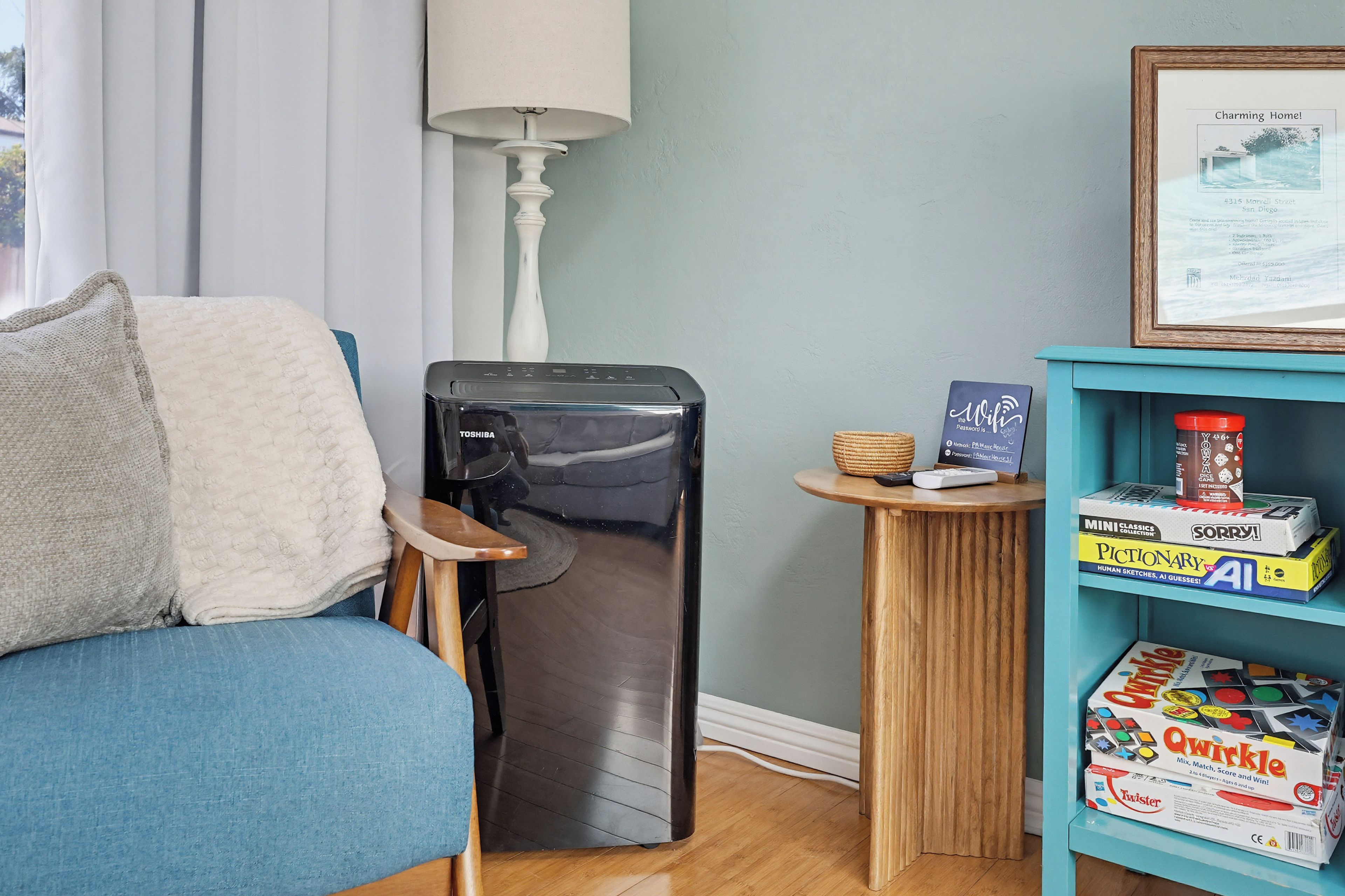 A compact living space with a blue sofa, a small refrigerator, a lamp, and a shelf with board games.