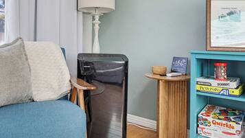 A compact living space with a blue sofa, a small refrigerator, a lamp, and a shelf with board games.
