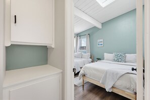 Une chambre à coucher avec un lit, une table de chevet, une fenêtre avec des rideaux et une étagère fixée au mur.