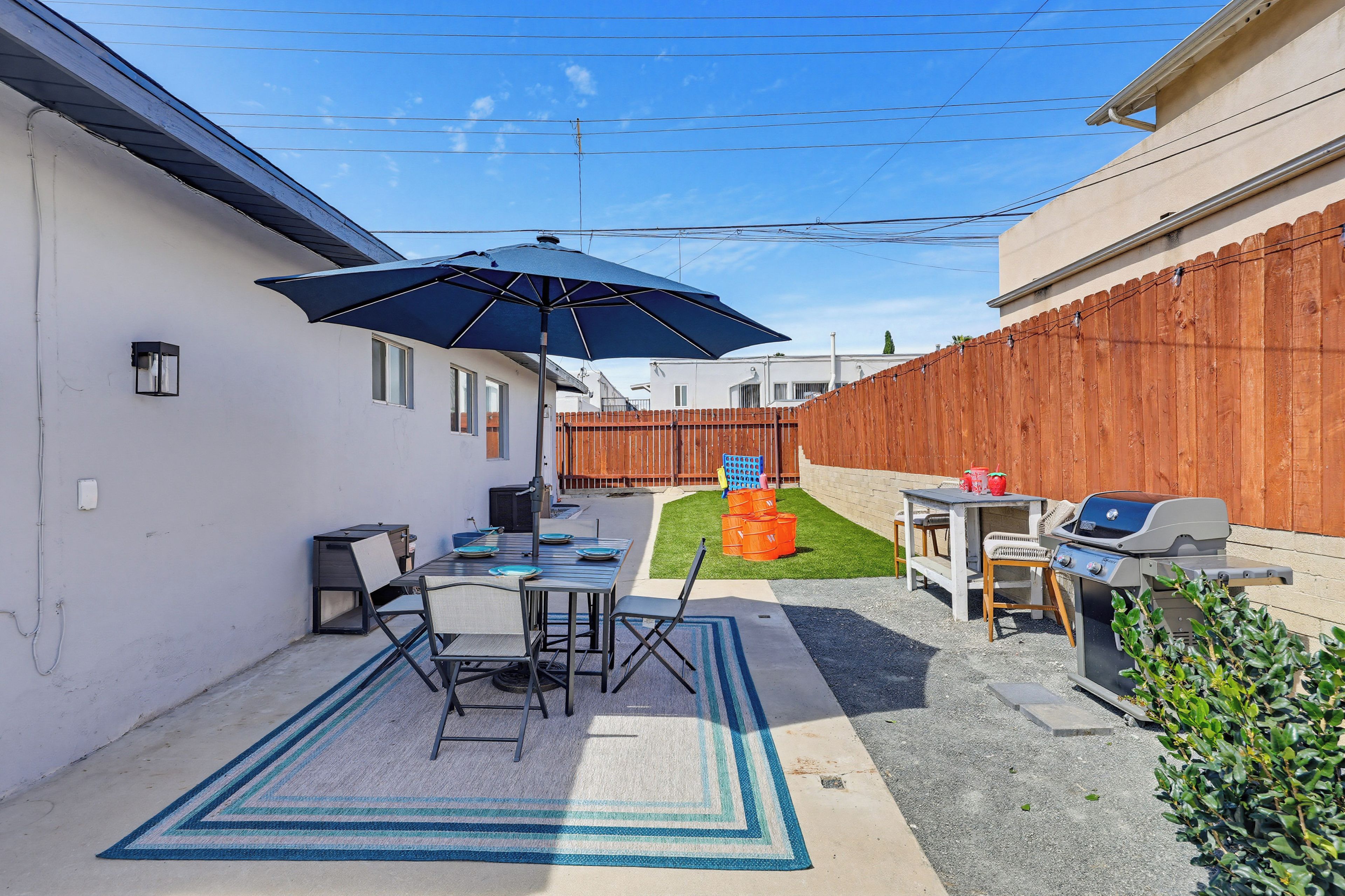 A backyard with a barbecue area, a table with chairs, and a blue umbrella.