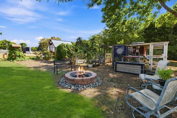 A backyard with a fire pit, outdoor seating, and a farmhouse-style structure.