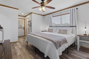 Ein Schlafzimmer mit einem Bett, Nachttischen, einem Deckenventilator und einem Fenster mit Vorhängen.