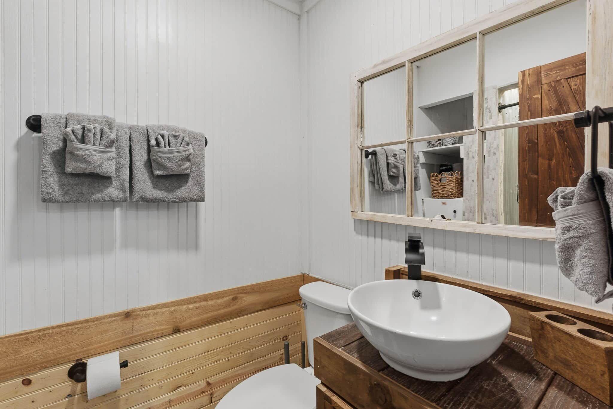 A bathroom with a wooden vanity, a white sink, a toilet, and towels hanging on the wall.