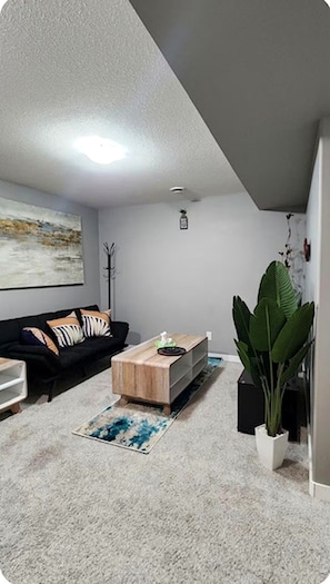 A living room with a black sofa, a wooden coffee table, a large green plant, and a painting on the wall. - A Cozy Gem in The Greens.
Welcome to your cozy home away from home in TheGreens! (Regina)