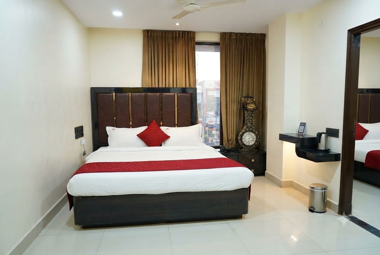 Une chambre d’hôtel avec un grand lit, une table de chevet, une horloge, un miroir et une fenêtre avec des rideaux.