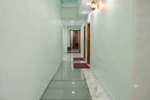 Un pasillo con suelo de vidrio, una puerta de madera y una lámpara fijada a la pared.