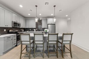 A modern kitchen with grey cabinetry, stainless steel appliances, and a central island with bar stools. - Jambalaya Row | 3 Private Homes | 7BR | Sleeps 15 (Lafayette)