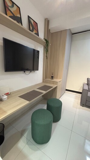 A modern living room with a flat-screen TV mounted on the wall, a wooden coffee table, two green ottomans, and a grey sofa. - Modern studio/apartment in Tatuapé - excellent location! (São Paulo)