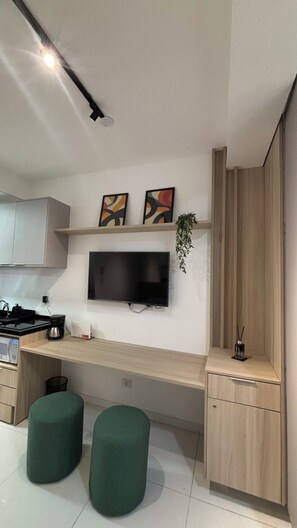 A modern kitchen with a flat-screen TV, wooden cabinets, and green stools. - Modern studio/apartment in Tatuapé - excellent location! (São Paulo)