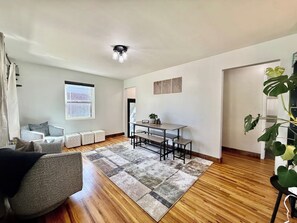 A living room with a sofa, a dining table with benches, a large plant, and a ceiling light fixture. - Rose Park Cottage | Near Downtown | Mid-Term (Salt Lake City)