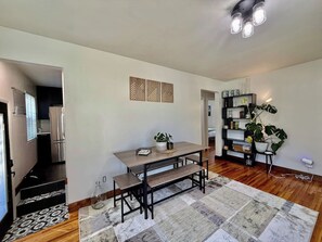 A dining area with a wooden table and benches, a patterned rug, and a bookshelf with plants. - Rose Park Cottage | Near Downtown | Mid-Term (Salt Lake City)