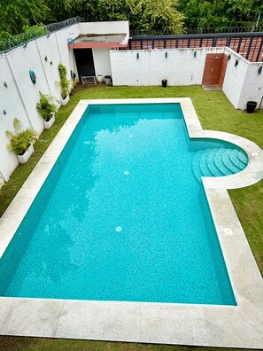 Ein rechteckiger Pool mit abgerundeter Kante, umgeben von einer weißen Mauer und einer kleinen Rasenfläche.