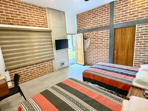 A room with a brick wall, a sliding door, a bed with patterned bedding, and a television mounted on the wall. - 5-SUITE VACATION HOME WITH A LARGE PRIVATE POOL (Cruz de Huanacaxtle)