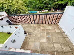 Eine Dachterrasse mit Backsteinboden, Metallgeländer und Blick auf ein blaues Boot im Hintergrund.