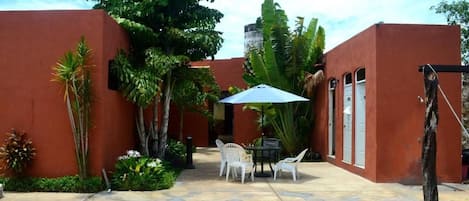 Piscina com mesa e cadeiras, rodeada por paredes vermelhas e plantas tropicais.