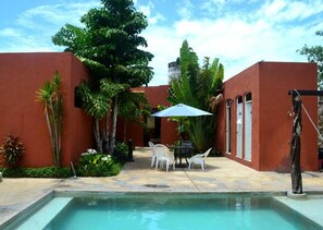 Una piscina con mesa y sillas, rodeada de paredes rojas y plantas tropicales.