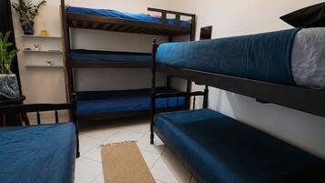 A dormitory room with bunk beds, a small table, a potted plant, and a light fixture.