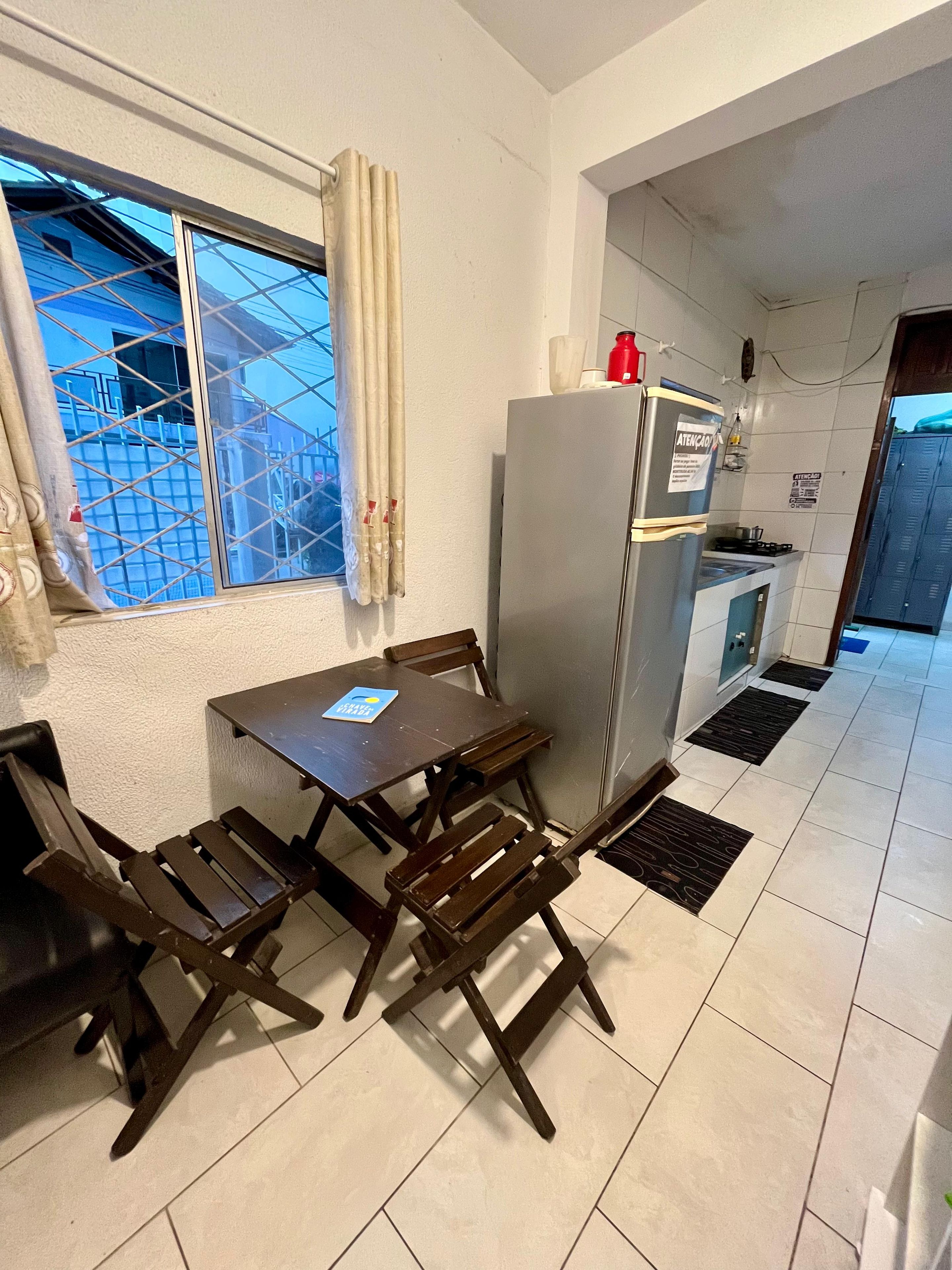 A compact kitchen with a refrigerator, a dining table with chairs, and a window with curtains.