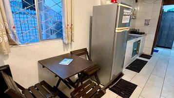 A compact kitchen with a refrigerator, a dining table with chairs, and a window with curtains.
