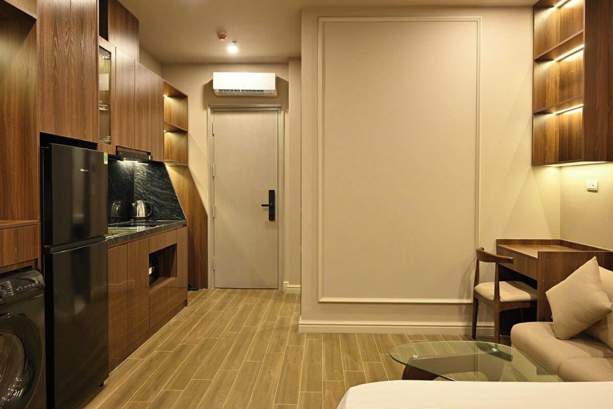 Cozinha compacta com geladeira, micro-ondas e máquina de lavar. Na sala de estar, há uma mesa de vidro e um sofá.