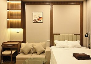 Quarto de hotel com cama, sofá, escrivaninha e luminária.