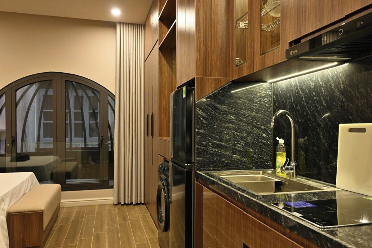 Uma cozinha compacta com máquina de lavar embutida, pia e janela com cortinas.
