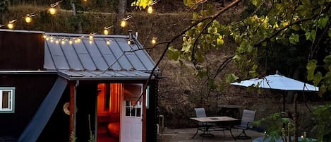 A rustic cabin with a wooden deck, a small outdoor seating area, and string lights.