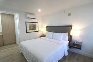 A hotel room with a bed, two bedside lamps, a framed picture on the wall, an air conditioning unit, and a wardrobe. - Mustang Queen Bedroom in the Heart of SLO (San Luis Obispo)