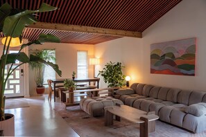 A modern living room with a sofa, a dining table, and various plants. - Creekside Austin Retreat. Sauna, Cold Plunge & Wooded Views (Austin)