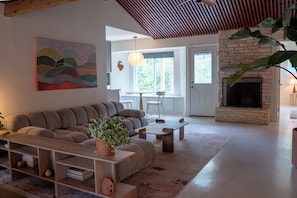 A modern living room with a sectional sofa, a coffee table, a bookshelf, and a fireplace. - Creekside Austin Retreat. Sauna, Cold Plunge & Wooded Views (Austin)