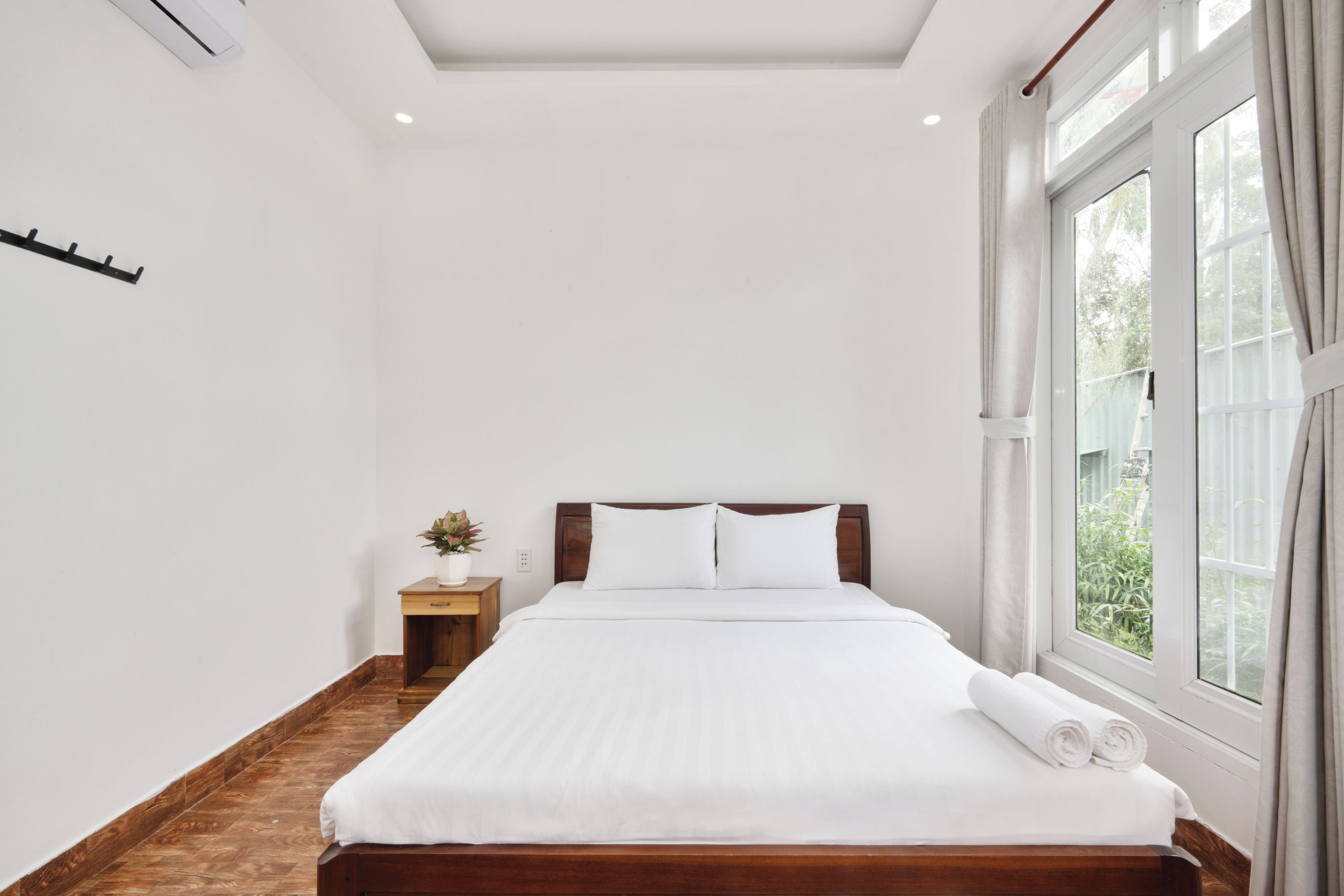Habitación de hotel con una cama grande, una mesita de noche, una planta en maceta y una ventana con cortinas.