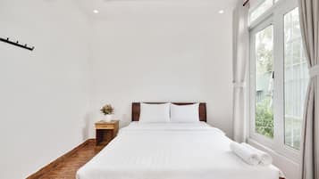 Habitación de hotel con una cama grande, una mesita de noche, una planta en maceta y una ventana con cortinas.