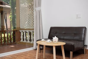 A room with a brown leather sofa, a wooden table with a teapot and cups, and a view of greenery outside.