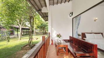 A room with a bed, a wooden bench, a table with teapots, and a view of a garden.