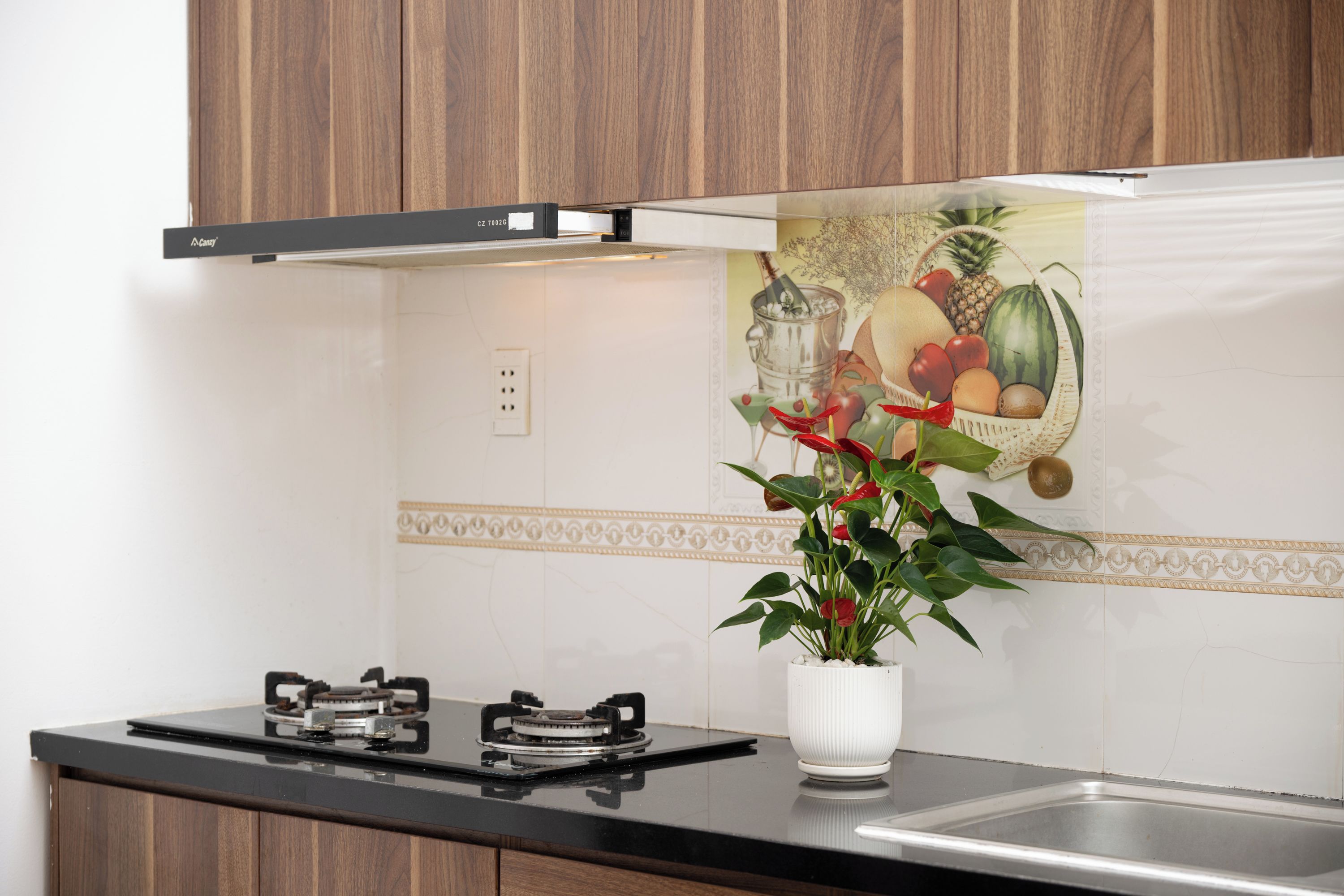 A kitchen with a gas stove, a white vase with a plant, and a wall with a fruit and vegetable mural.