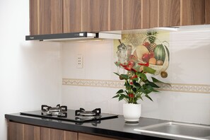 A kitchen with a gas stove, a white vase with a plant, and a wall with a fruit and vegetable mural.