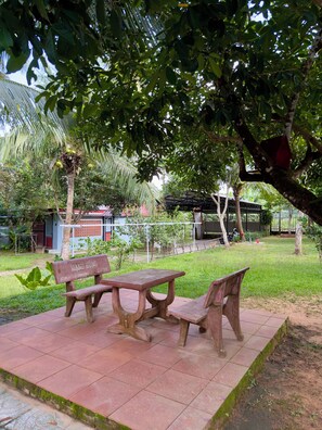 Un parque con una mesa de picnic y bancos, rodeado de árboles y una valla.