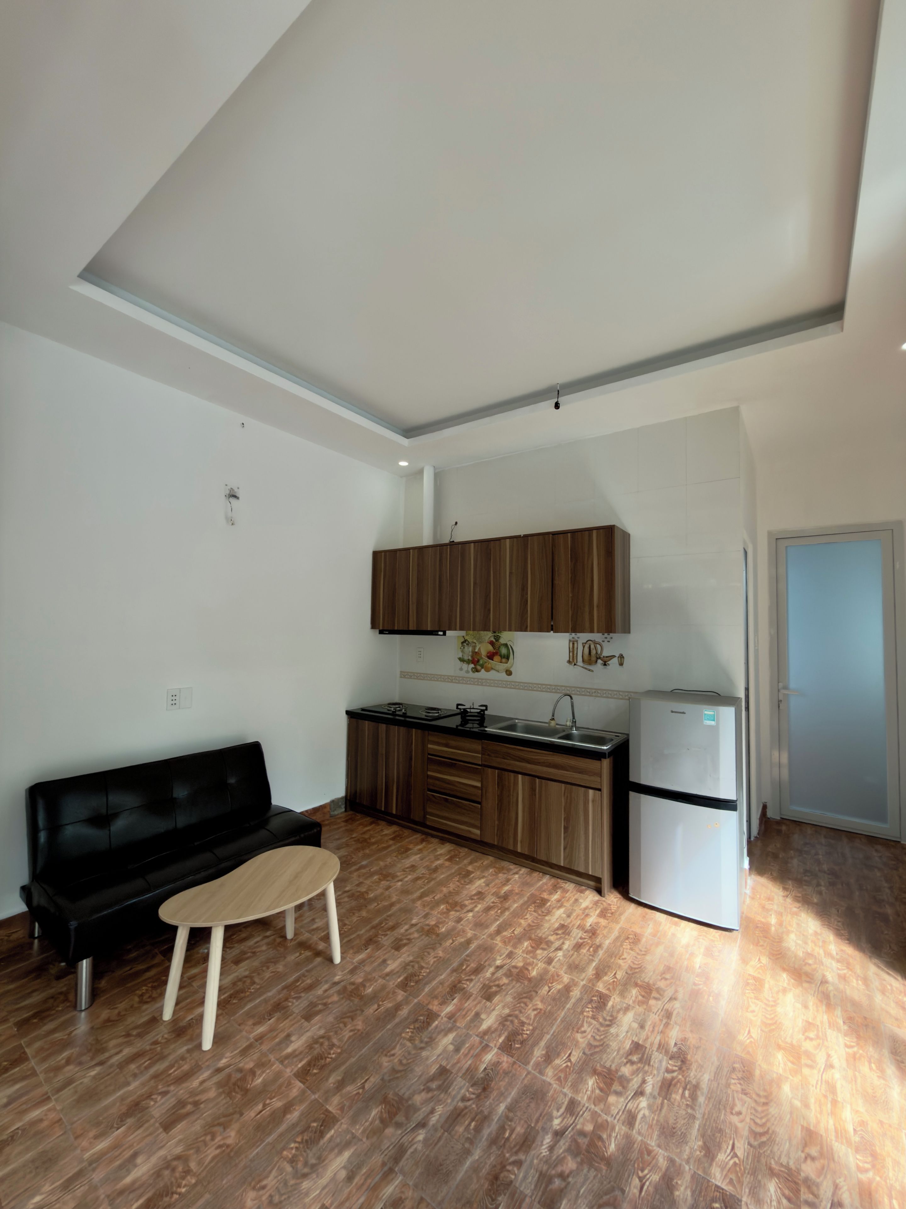 Una cocina compacta con armarios de madera, un sofá negro y una pequeña mesa de madera.