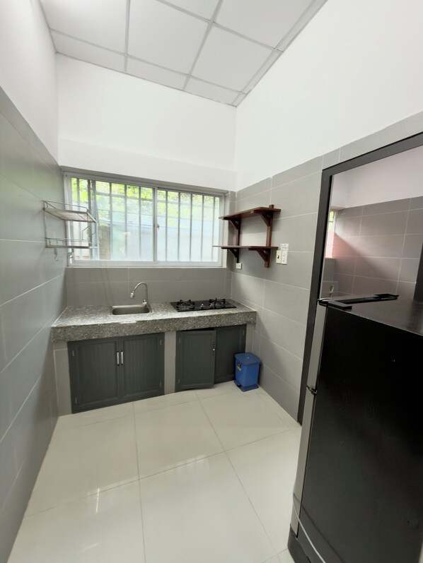 A compact kitchen with a window, a sink, cabinets, and a black refrigerator.