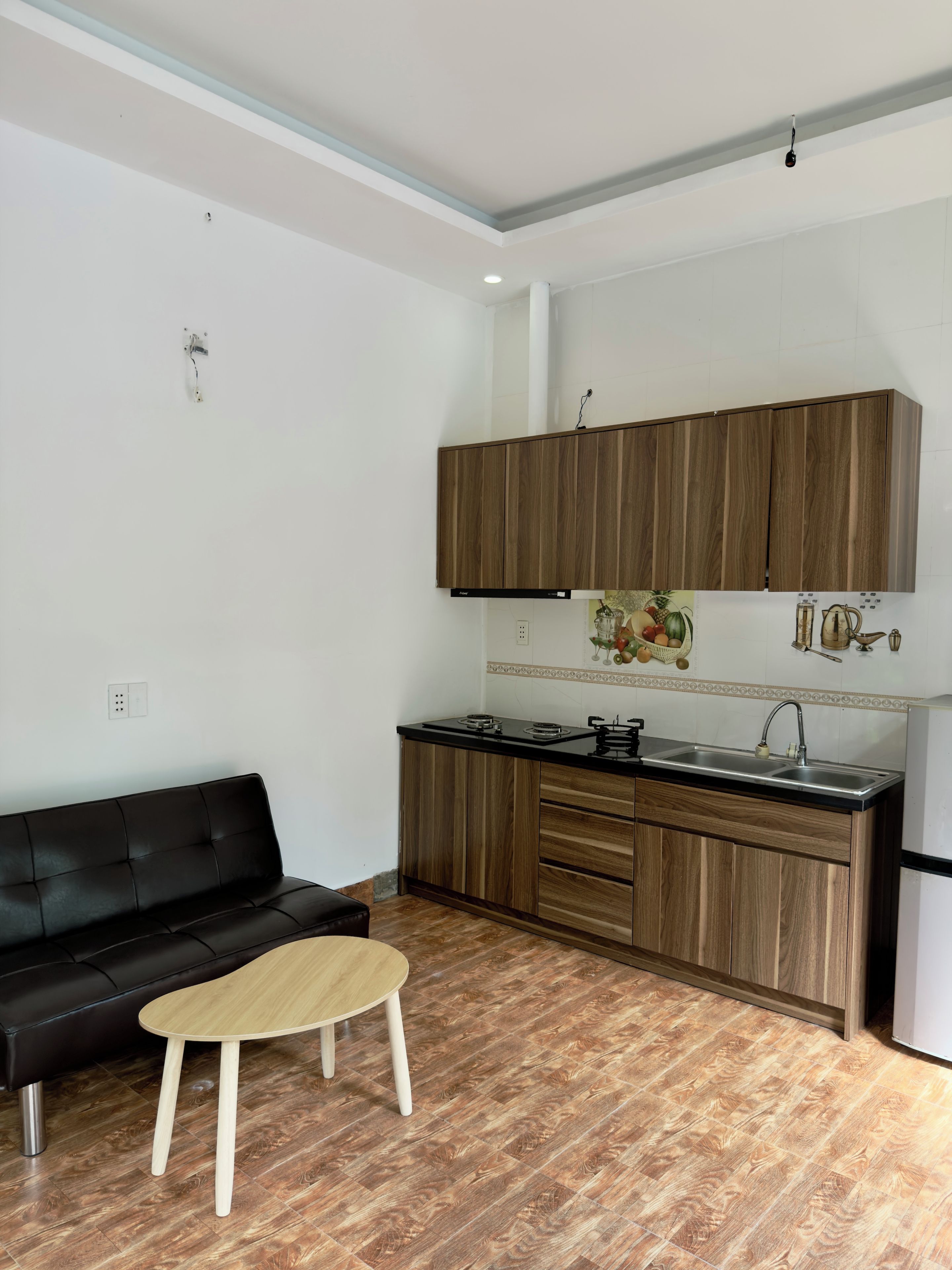 Een kleine keuken met houten kasten, een zwart aanrechtblad en een eethoekje met een houten tafel en een zwarte bank.