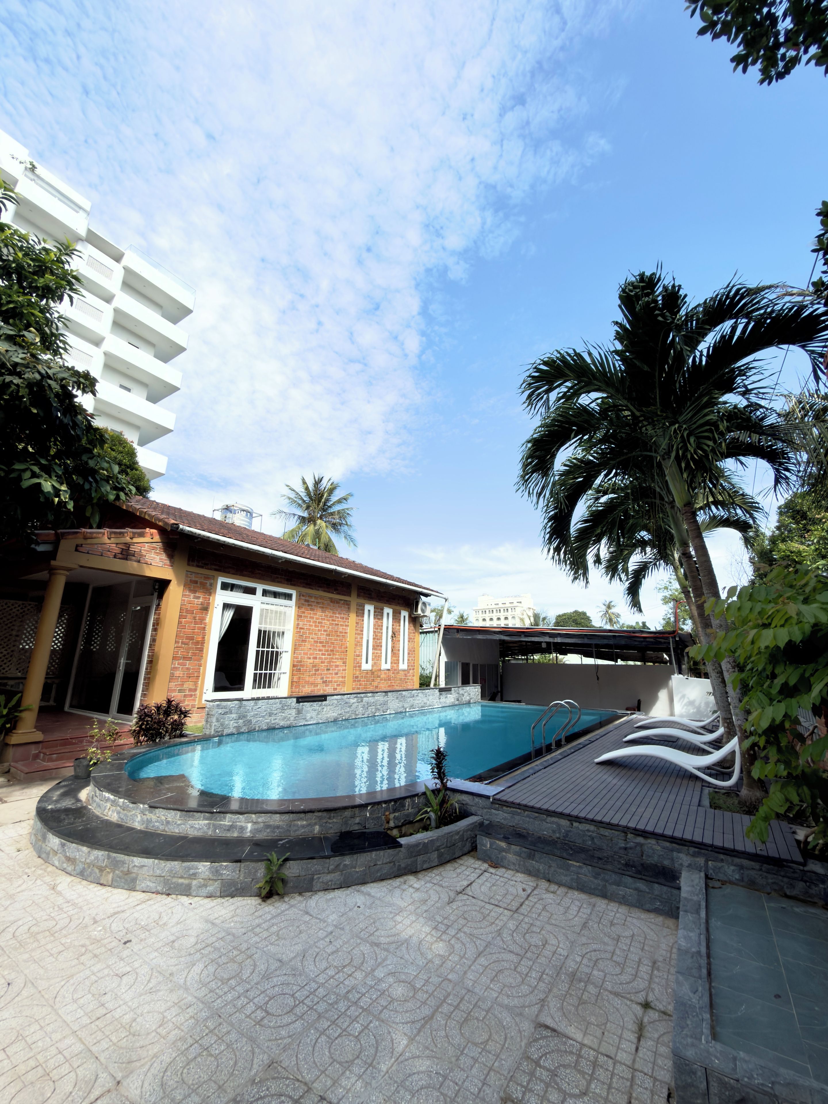 Zona de piscina con un edificio de ladrillo, palmeras y cielo despejado.