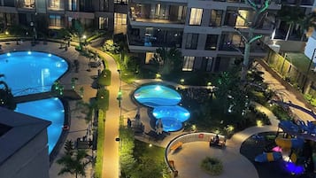 A multi-level hotel with a large outdoor swimming pool area, including a children's play area and multiple hot tubs.